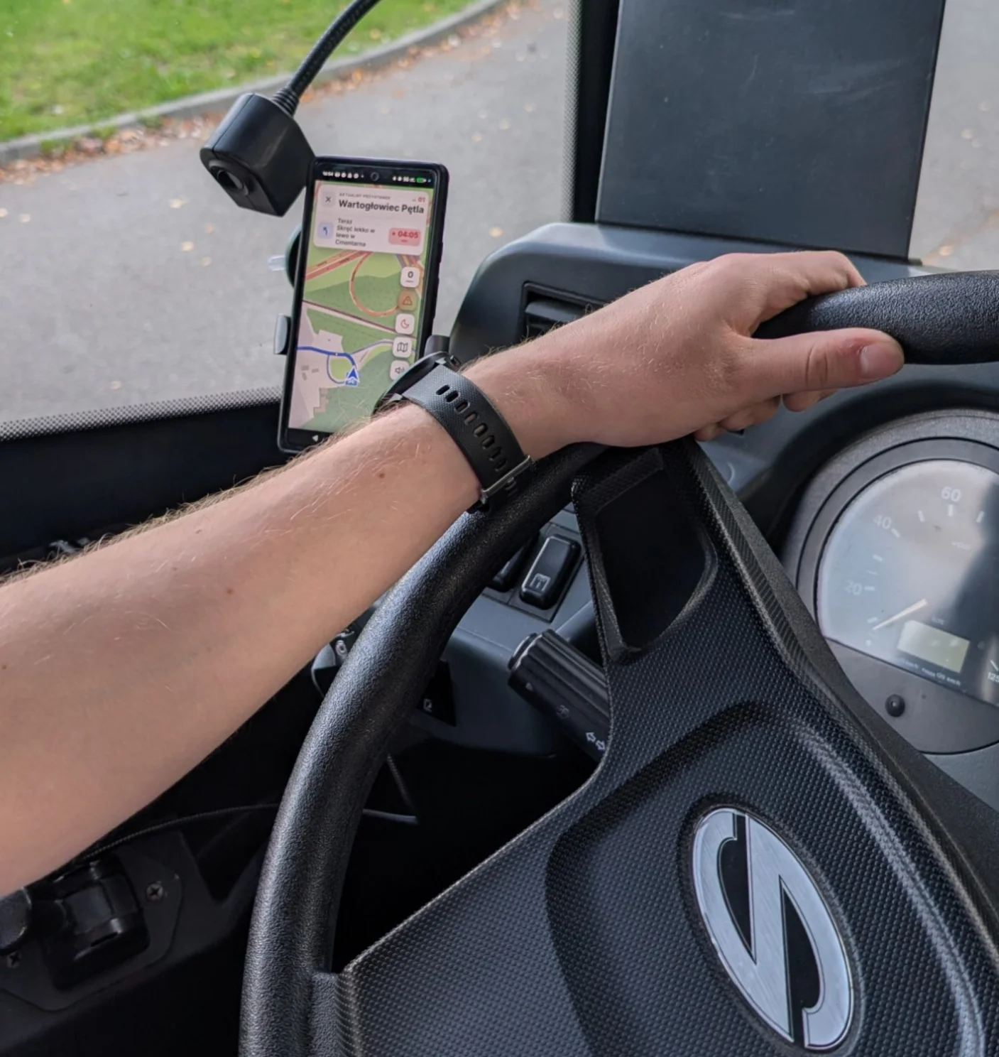 Kierowca autobusu z ręką na kierownicy, obok w uchwycie telefon z pilotem BusGo